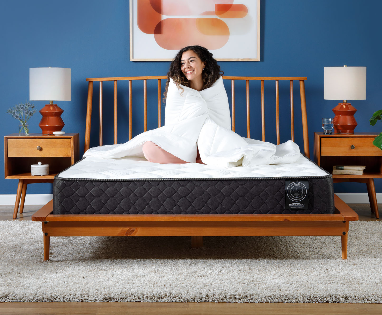 Woman sitting on Summit Firm Mattress in Bedroom wrapped in comforter