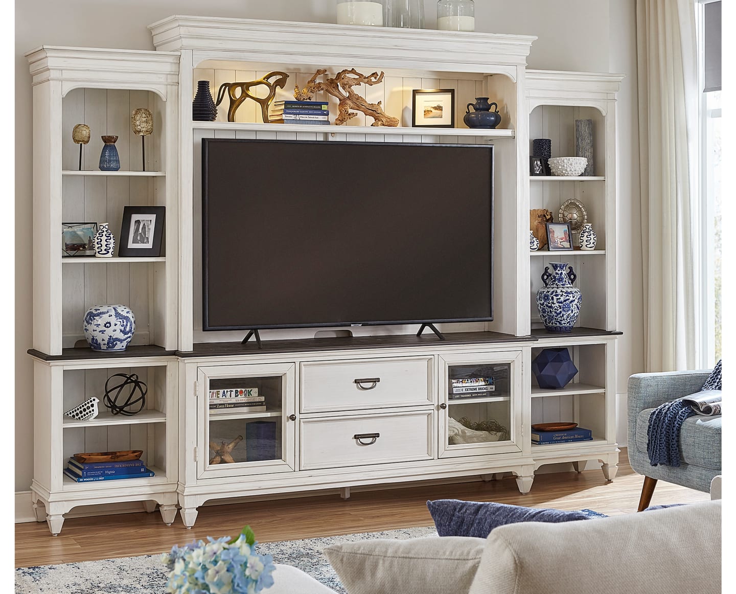 A large white entertainment center made from wood with a TV and coastal decor.