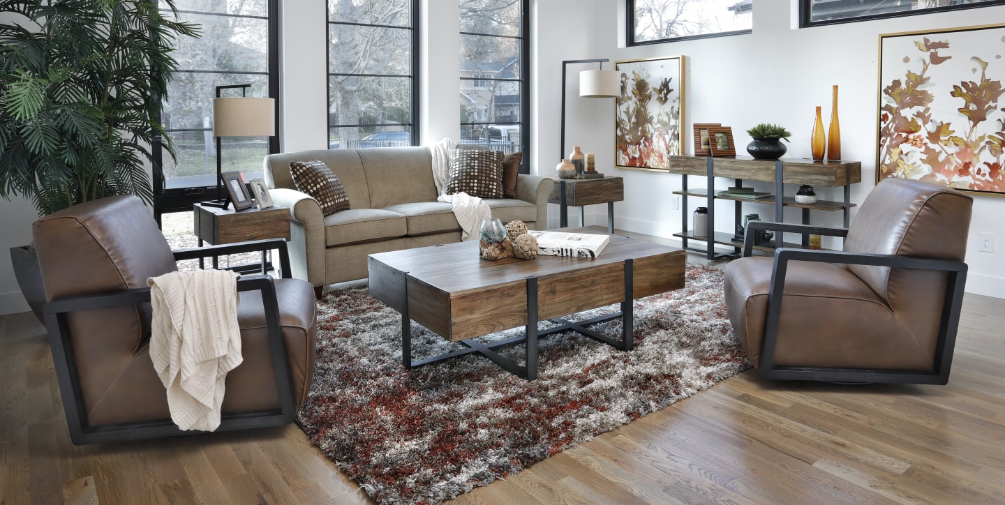 Casual fabric sofa with two leather swivel chairs around a rustic coffee table in warm toned living room window scene