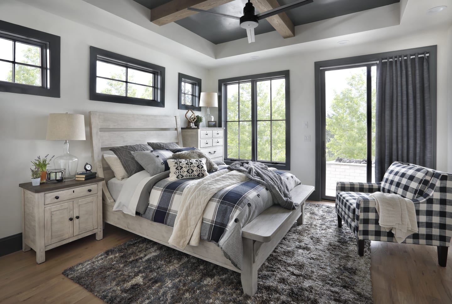 Cream colored farmhouse bedroom set with slatted headboard accompanied by matching nightstand and chest in bedroom window scene