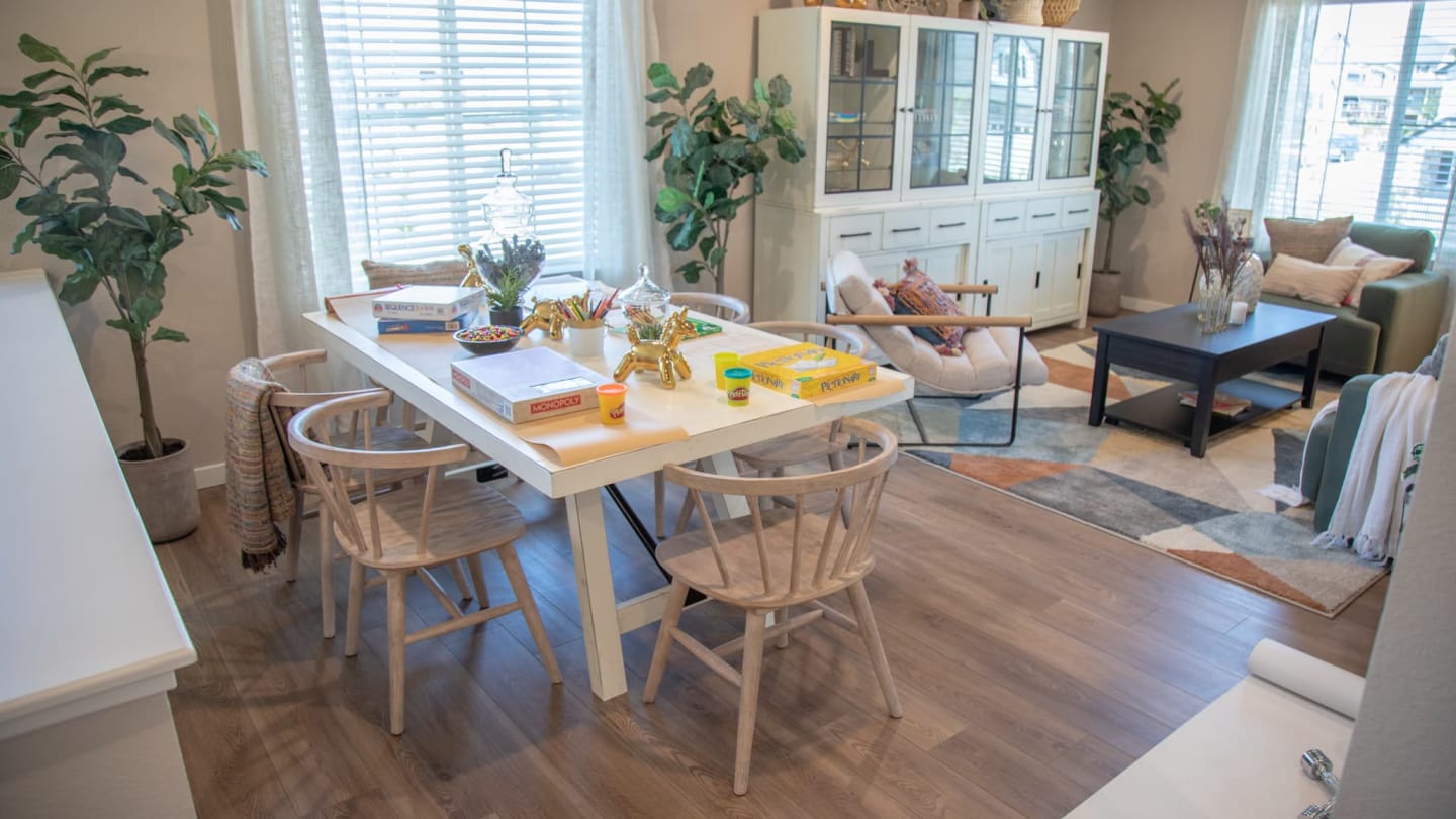 White rectangular La Paz Dining Table with games on top and surrounded by dining chairs in an open living space window scene