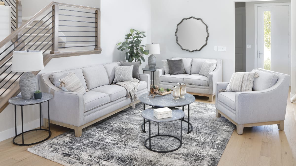 A light gray sofa, loveseat, and chair with exposed wood bases in a living room with round coffee tables