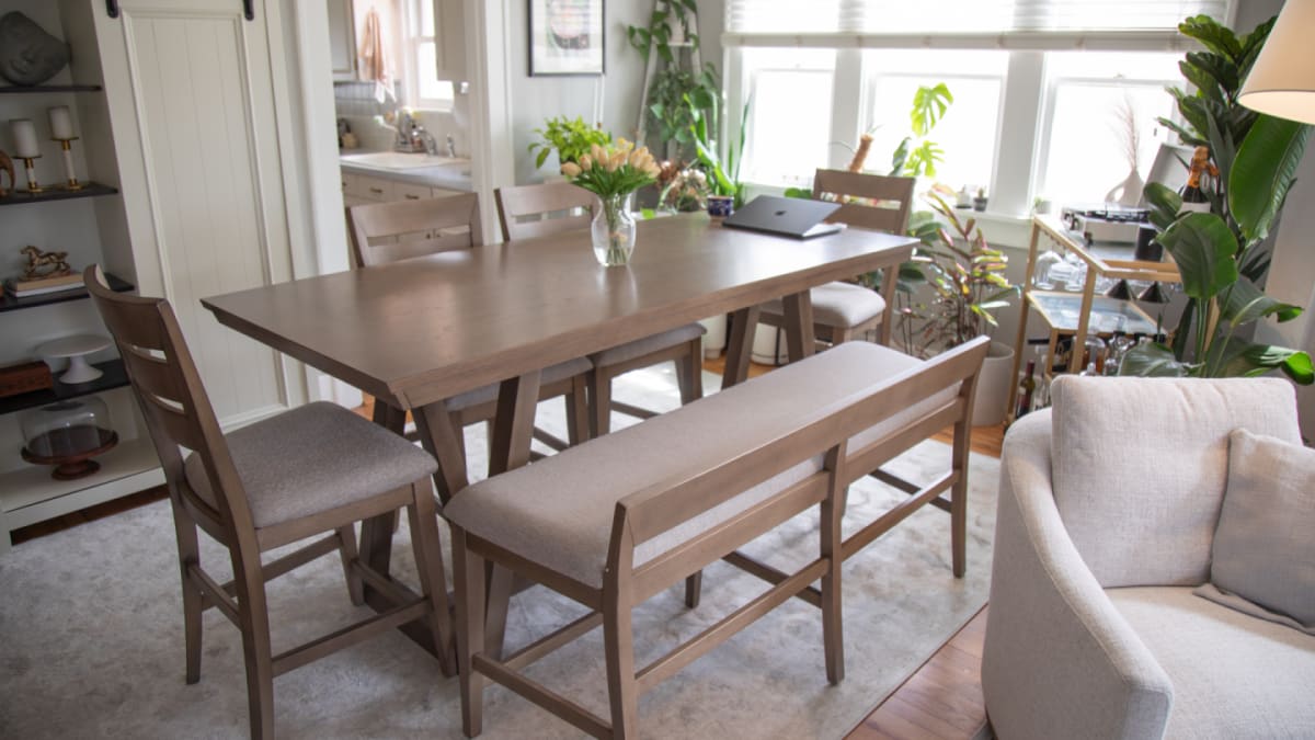 A counter height dining table with upholstered chairs in a dining room with plants