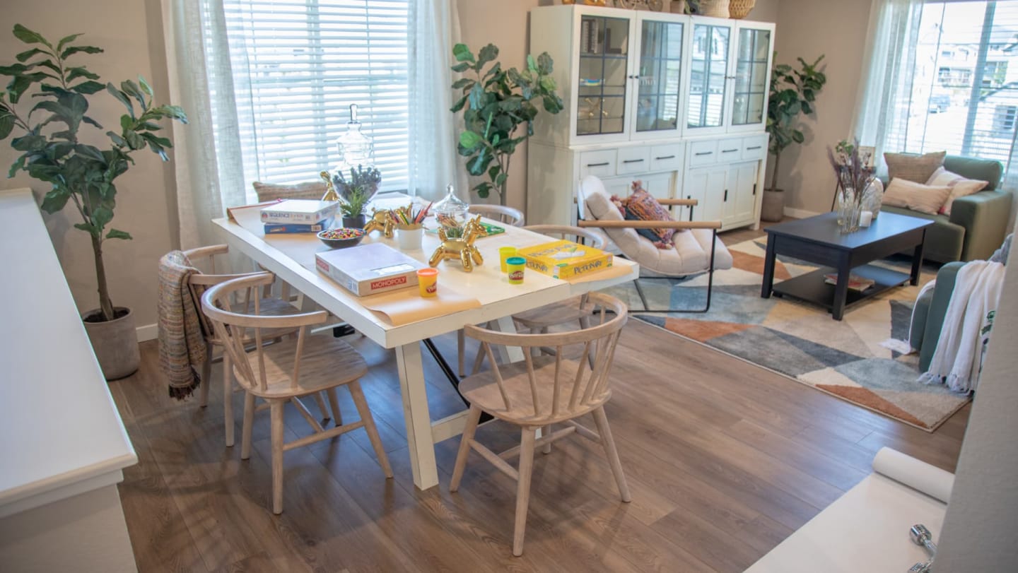 White rectangular La Paz Dining Table with games on top and surrounded by dining chairs in an open living space window scene