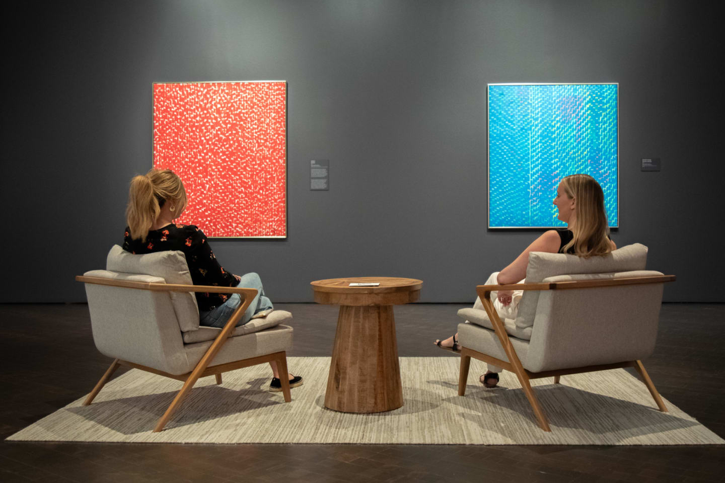 Wide shot of two people in the mid-century modern arm chairs with a round wood end table between them featured at the Denver Art Museum
