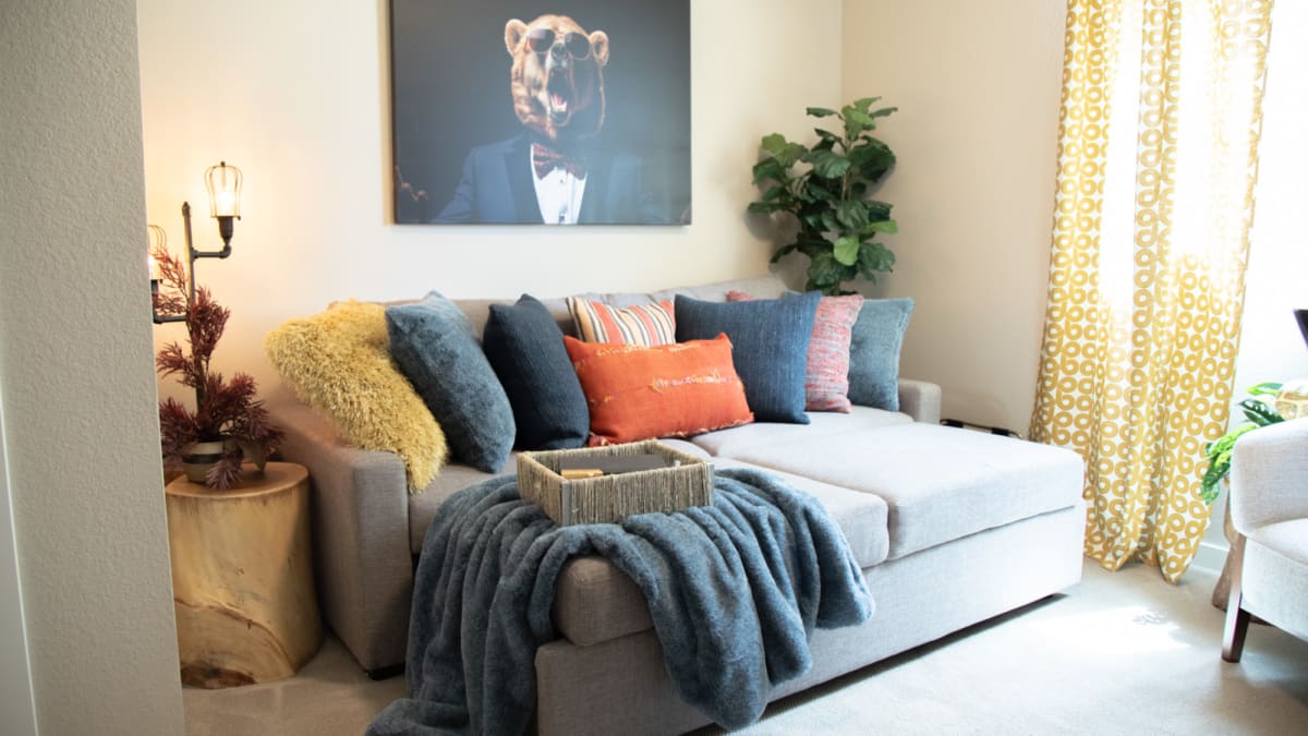 A small sofa with an extended sleeping chaise topped with pillows with comfy fabrics