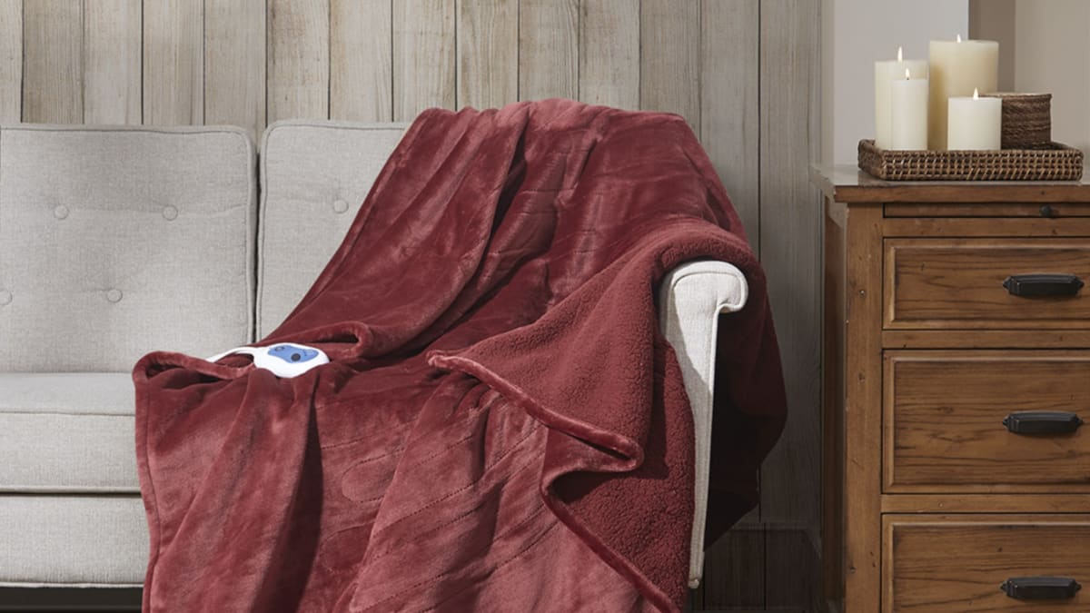 A plush, red heated throw blanket featured on a couch with its remote control