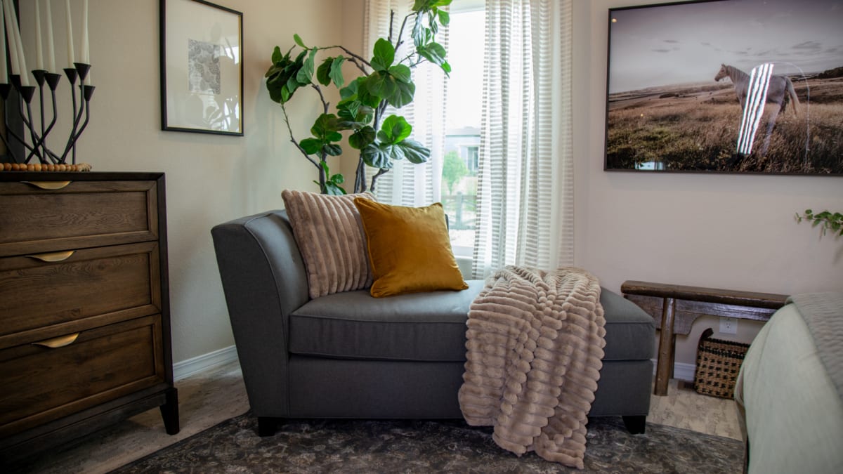 A small, armless chaise lounge topped with channeled pillows and blankets