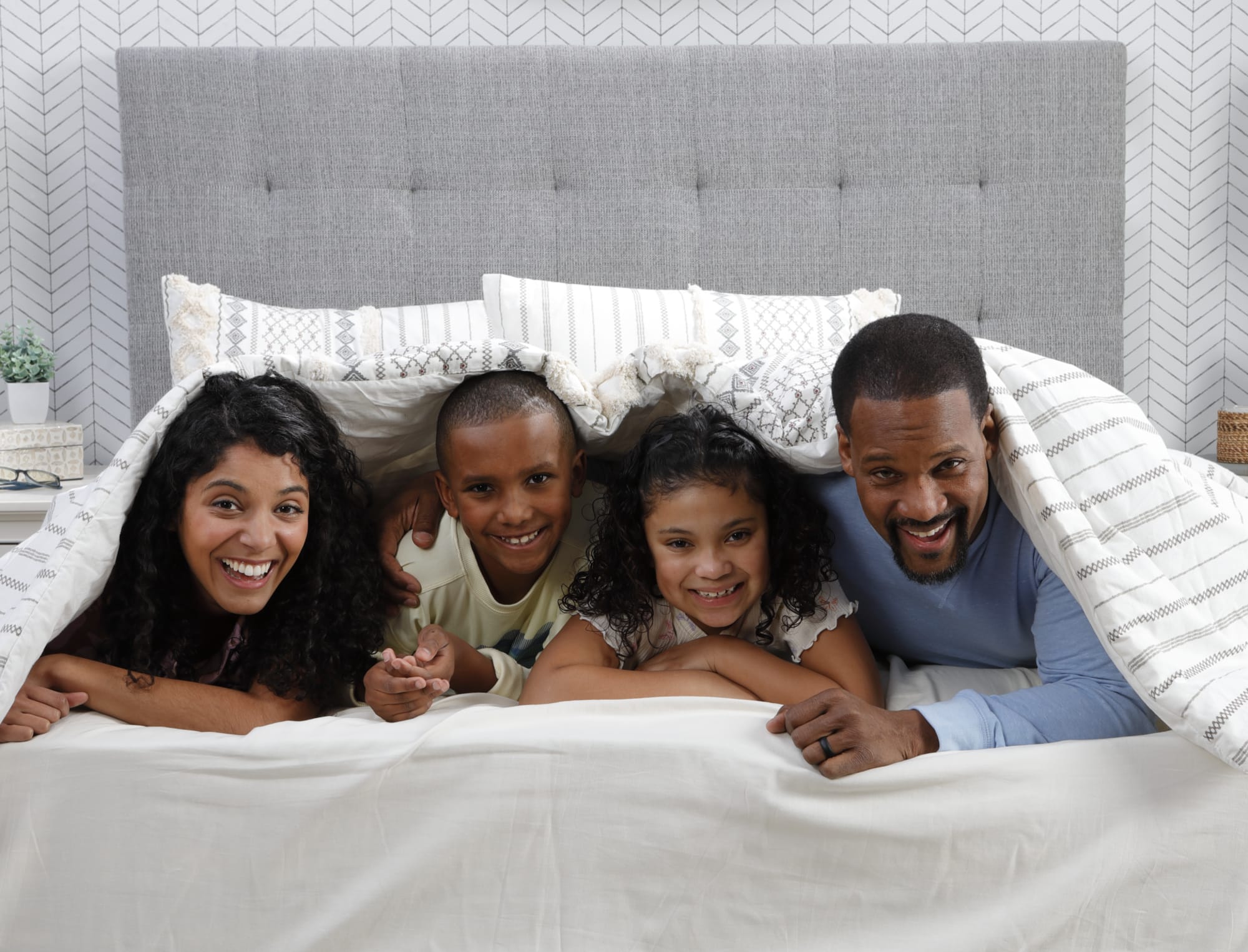 A family poking their heads out and smiling from under the covers on a bed