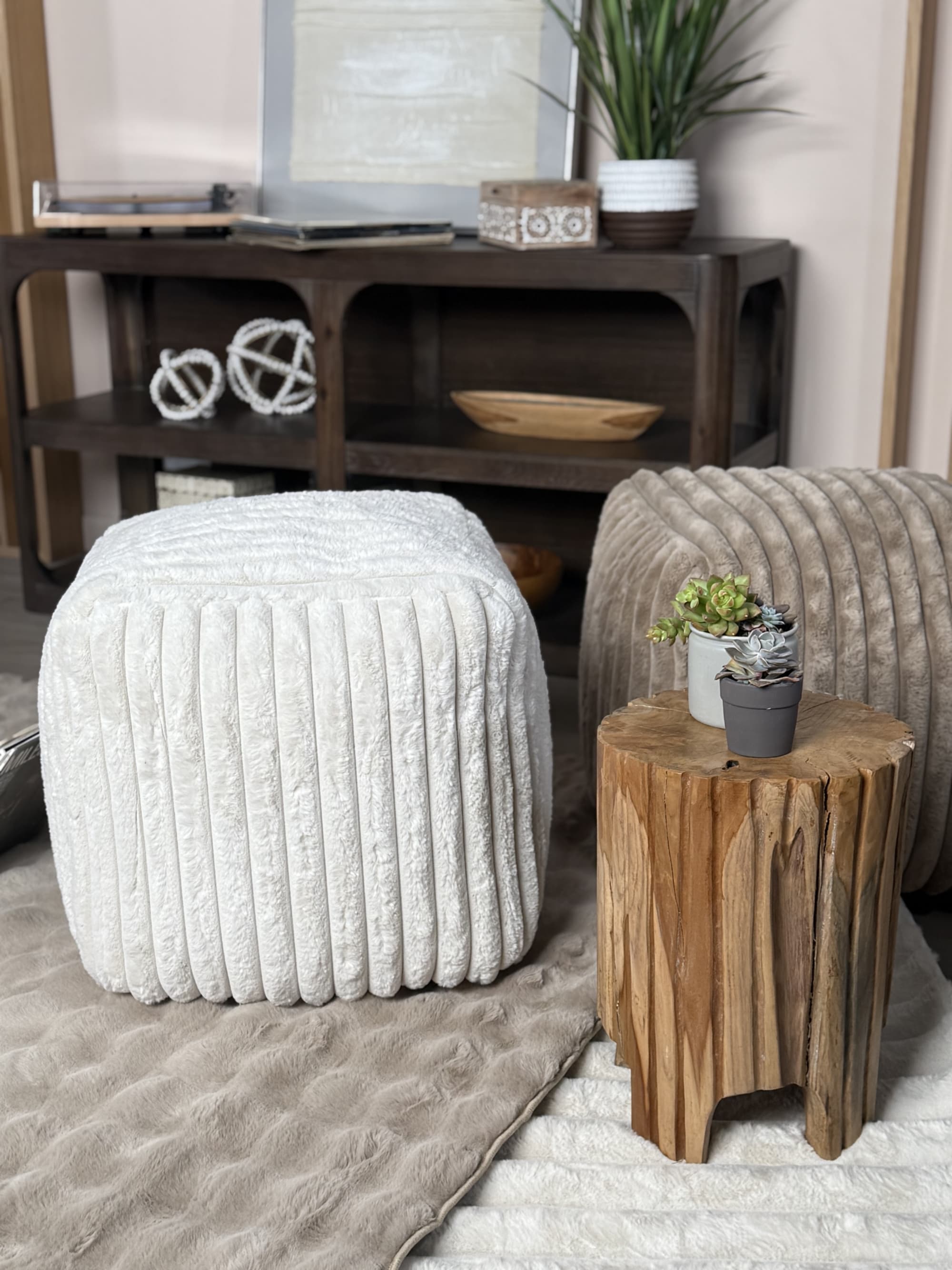 Two channeled pouf ottomans, one white one brown, on top of soft rugs in a living room
