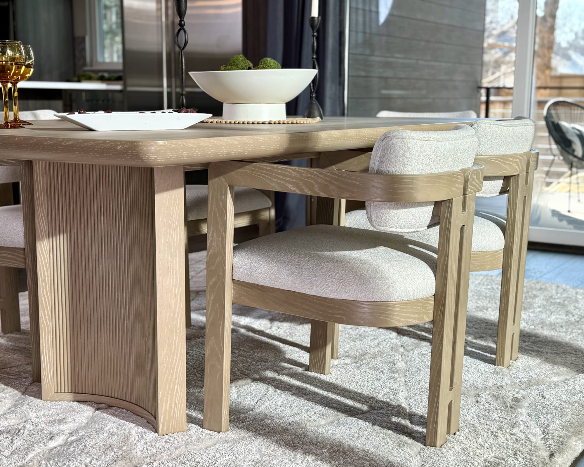 A contemporary light wood table with tambor pedestal legs, paired with round dining chairs with upholstered seats