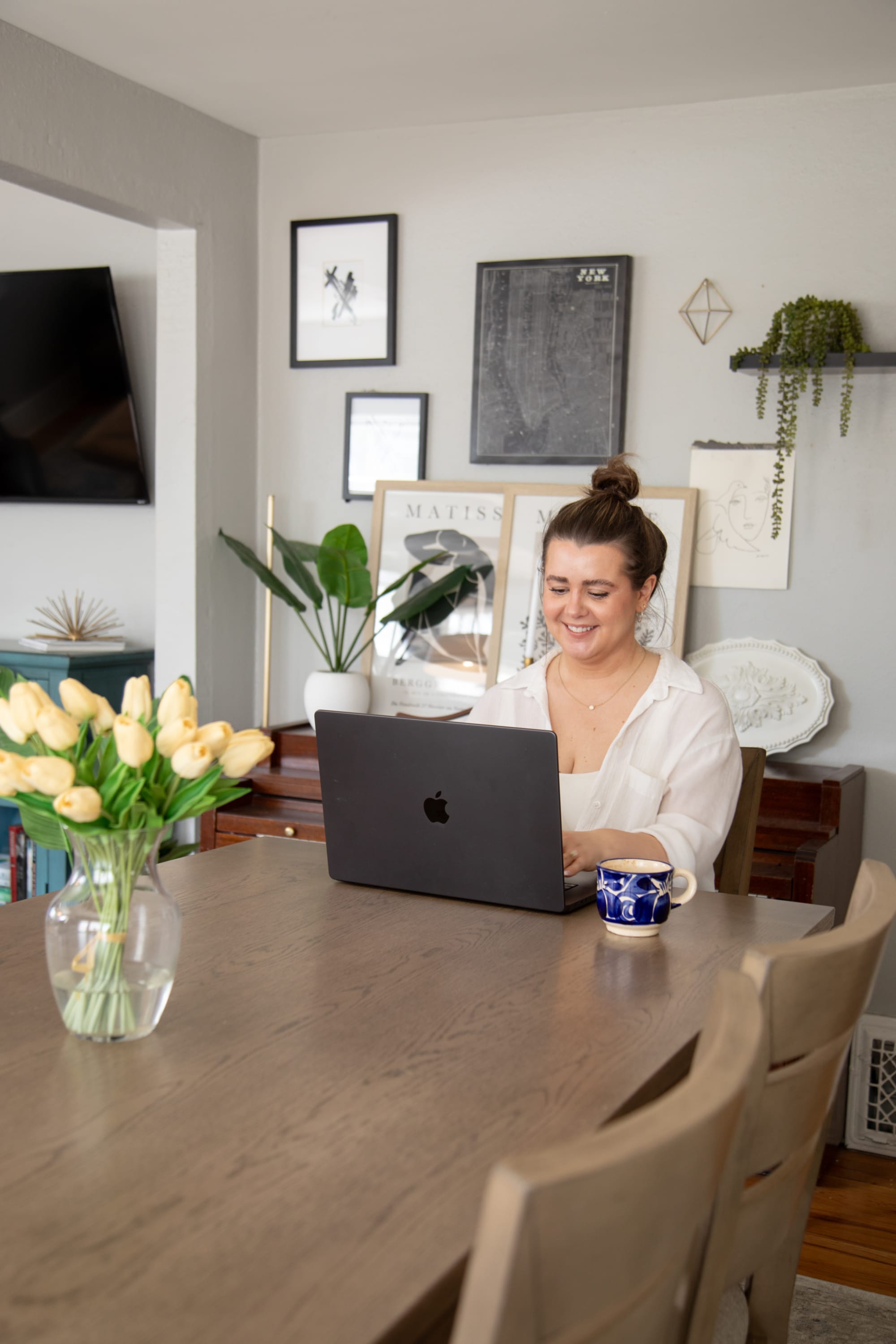A smiling woman sitting with her laptop at the modern wood Mesa Verde 5 Pc. Counter Height Dining Set in a dining room scene