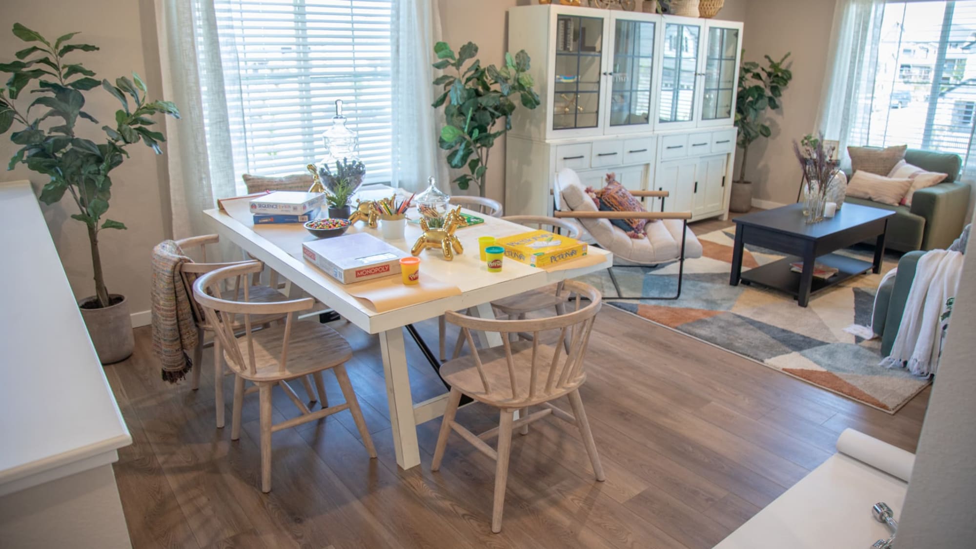 White rectangular La Paz Dining Table with games on top and surrounded by dining chairs in an open living space window scene