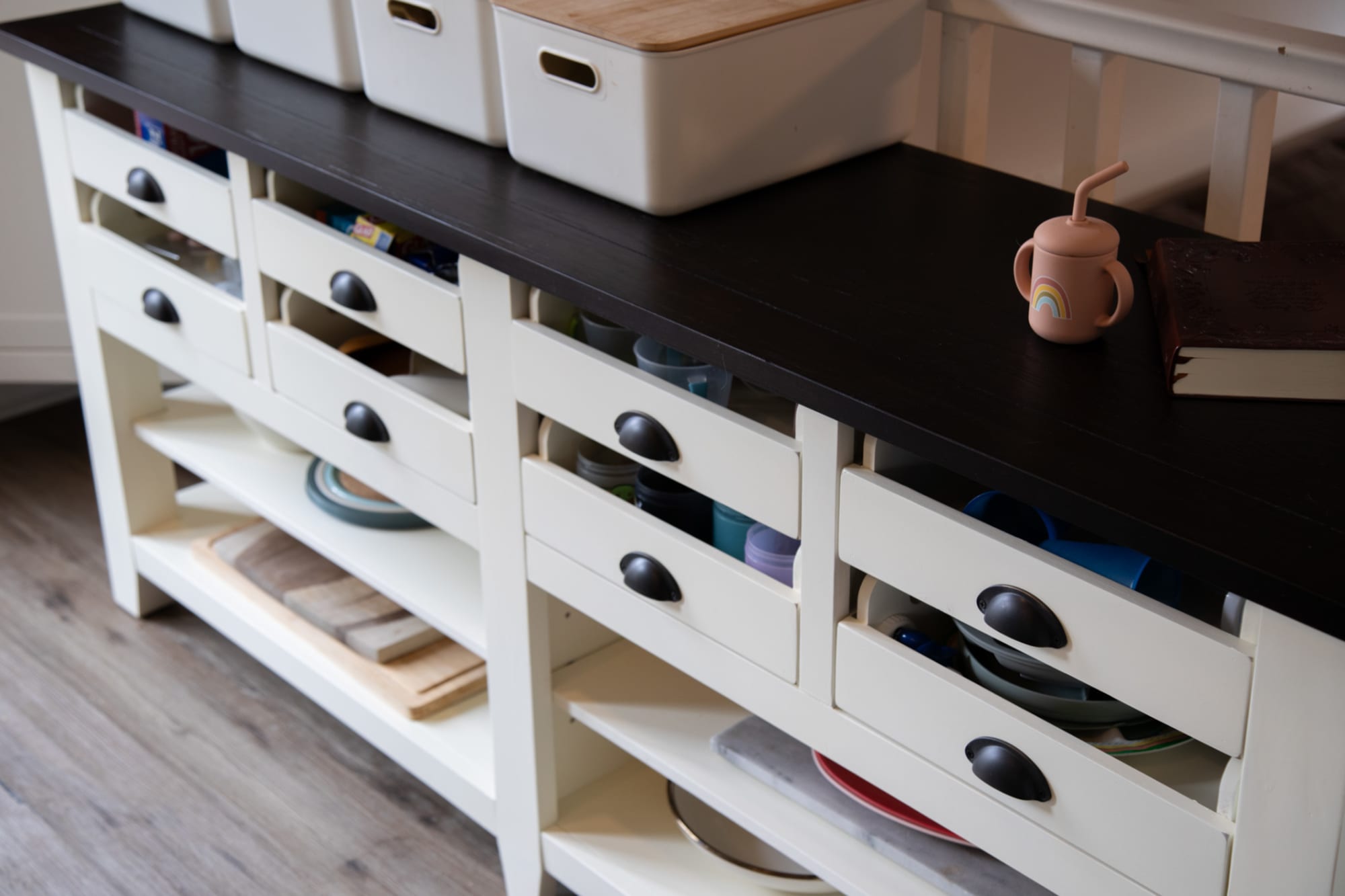 A white wood credenza with a dark top in a kitchen space holding toddler plates