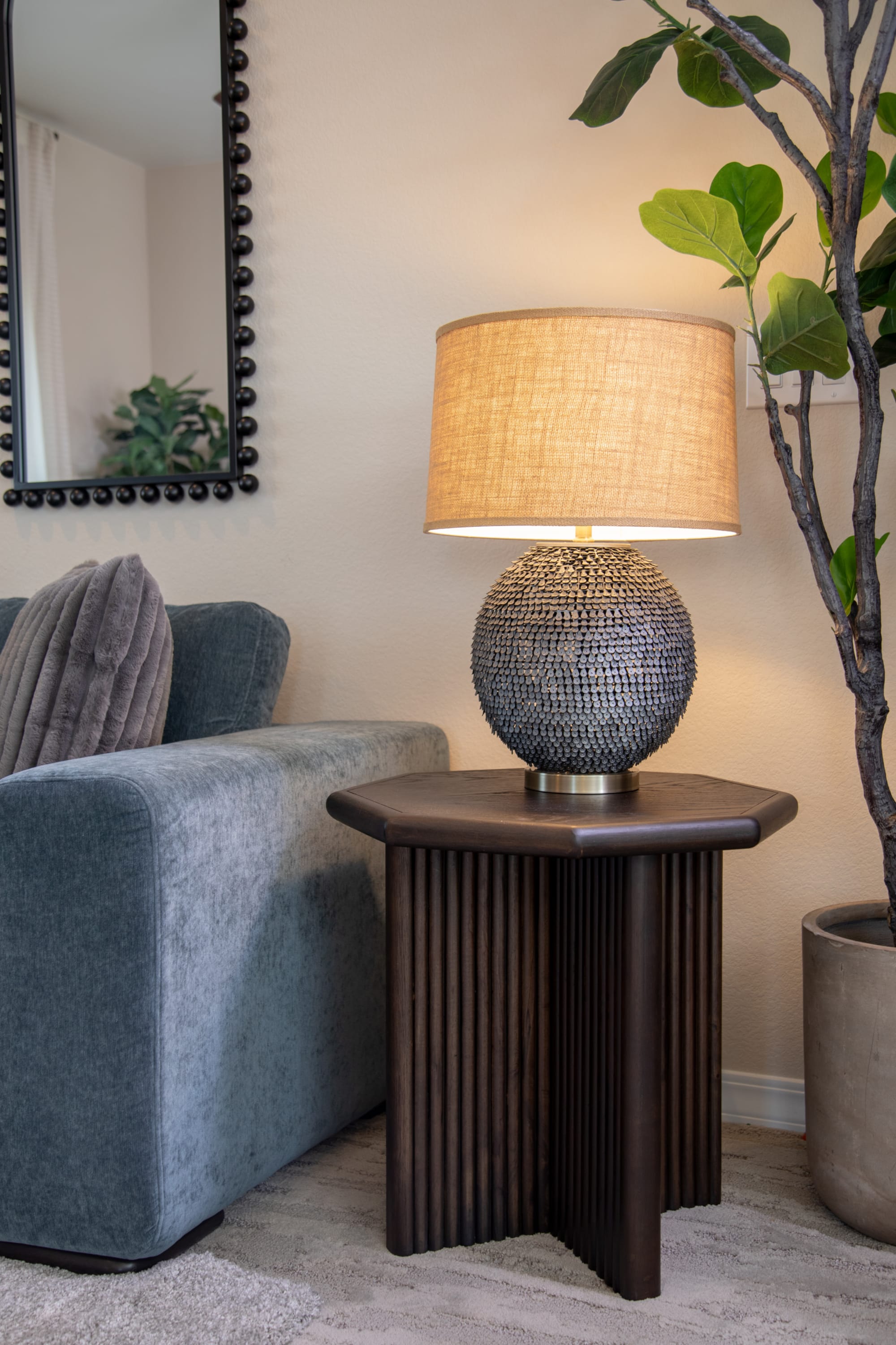 A hexagonal wood end table with a round metallic table lamp, illuminated