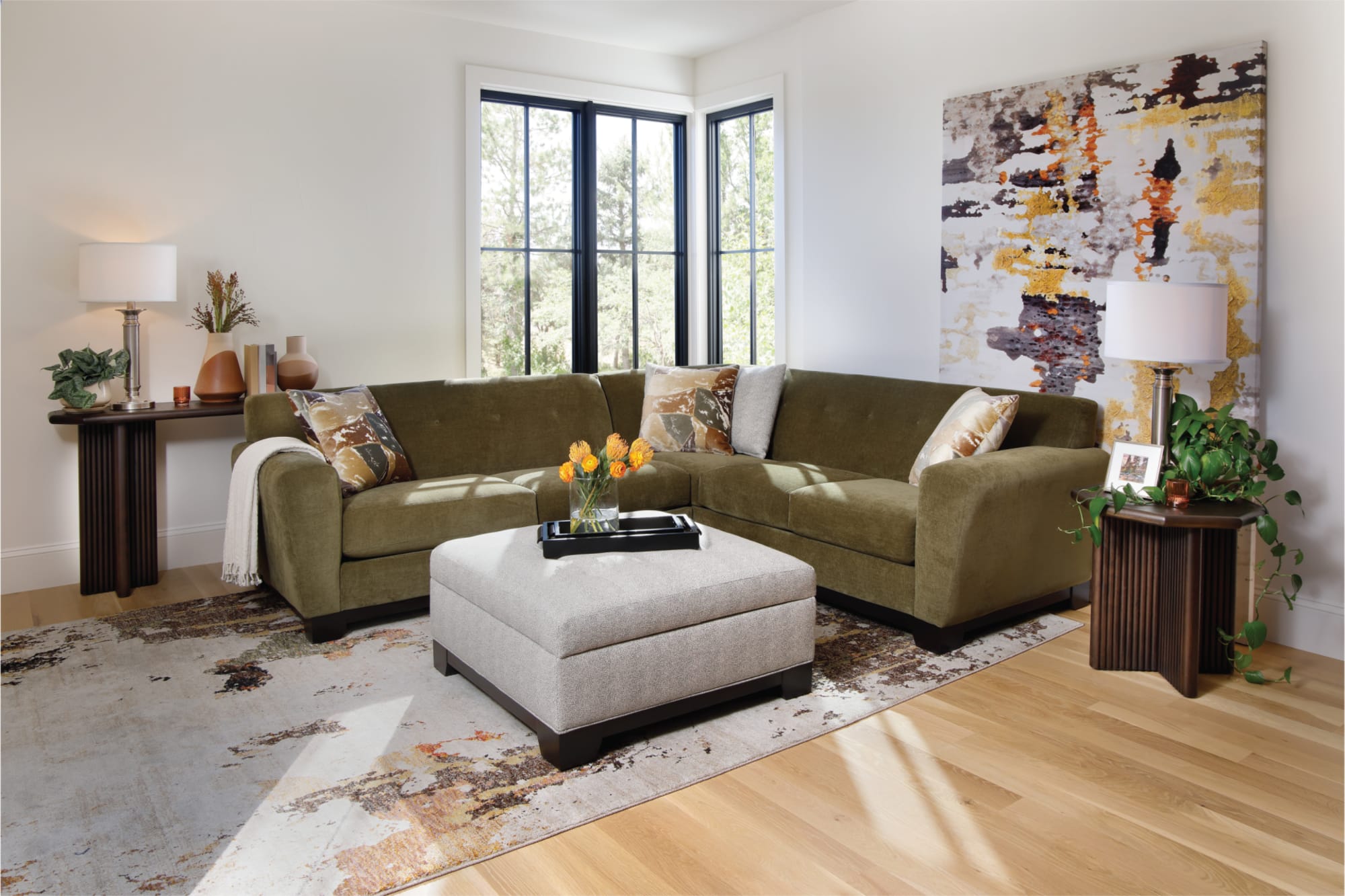 Green sofa with gray ottoman. Decorated with yellow flowers and accent pillows.