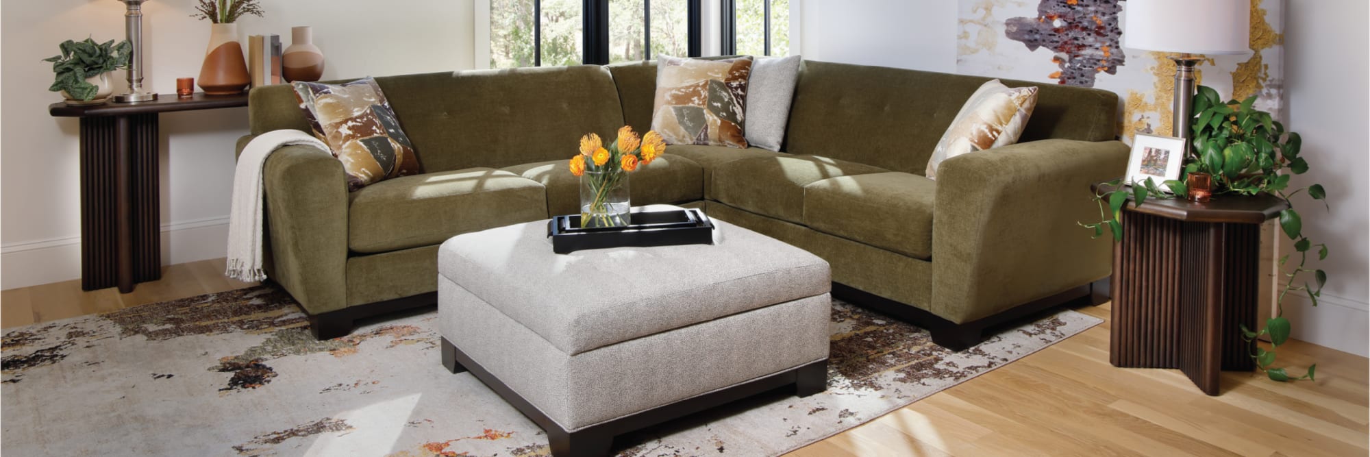 Green sofa with gray ottoman. Decorated with yellow flowers and accent pillows.