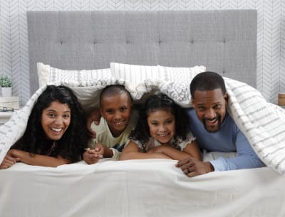 A family poking their heads out and smiling from under the covers on a bed