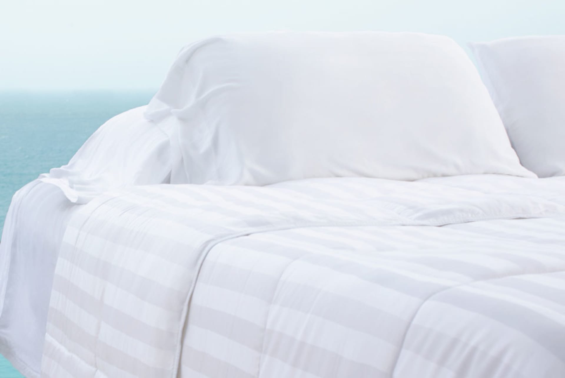 White Comforter and Pillowcases on bed with ocean in the background