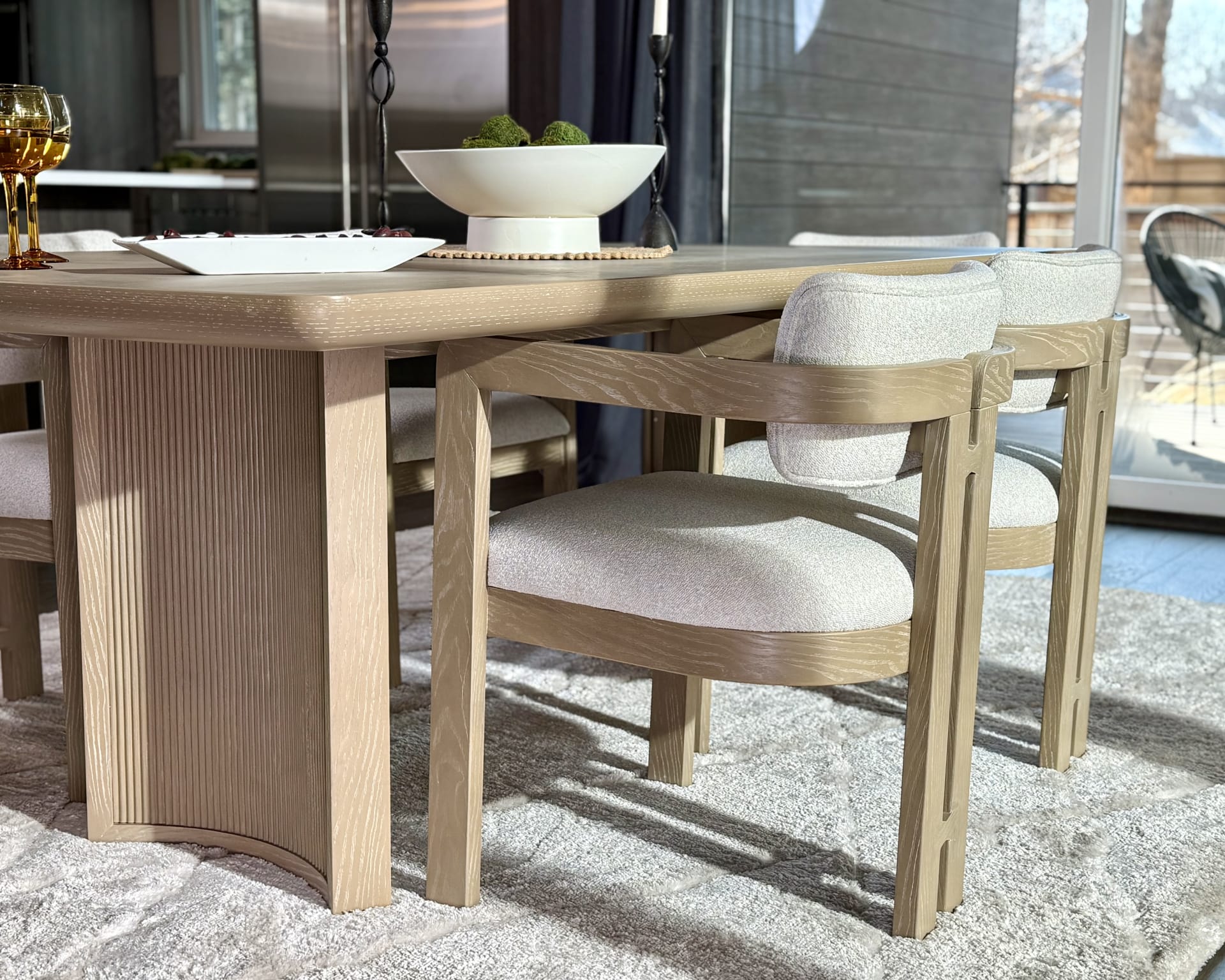 A contemporary light wood table with tambor pedestal legs, paired with round dining chairs with upholstered seats