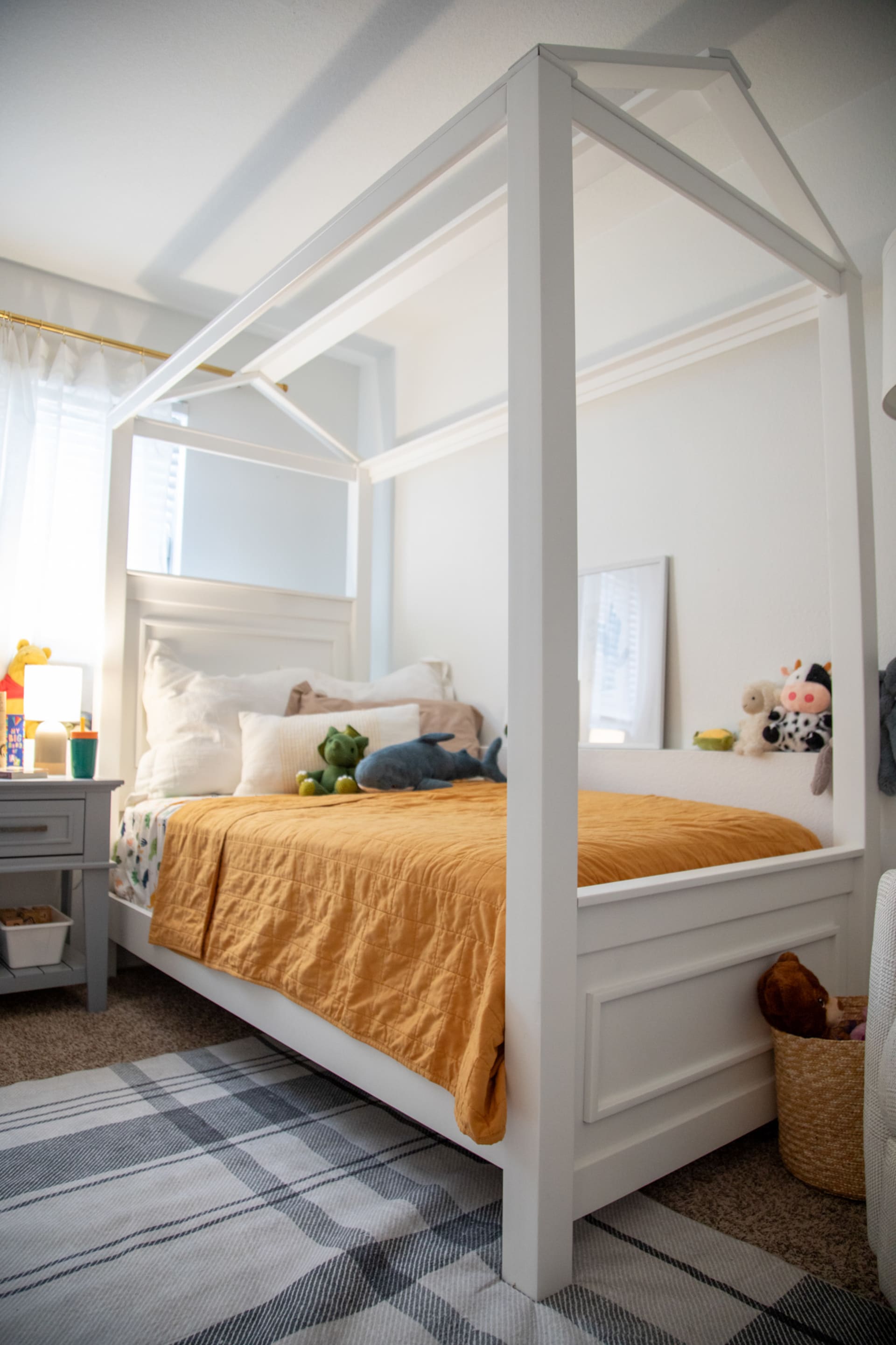 A white canopy bed with a gray nightstand in a kids bedroom
