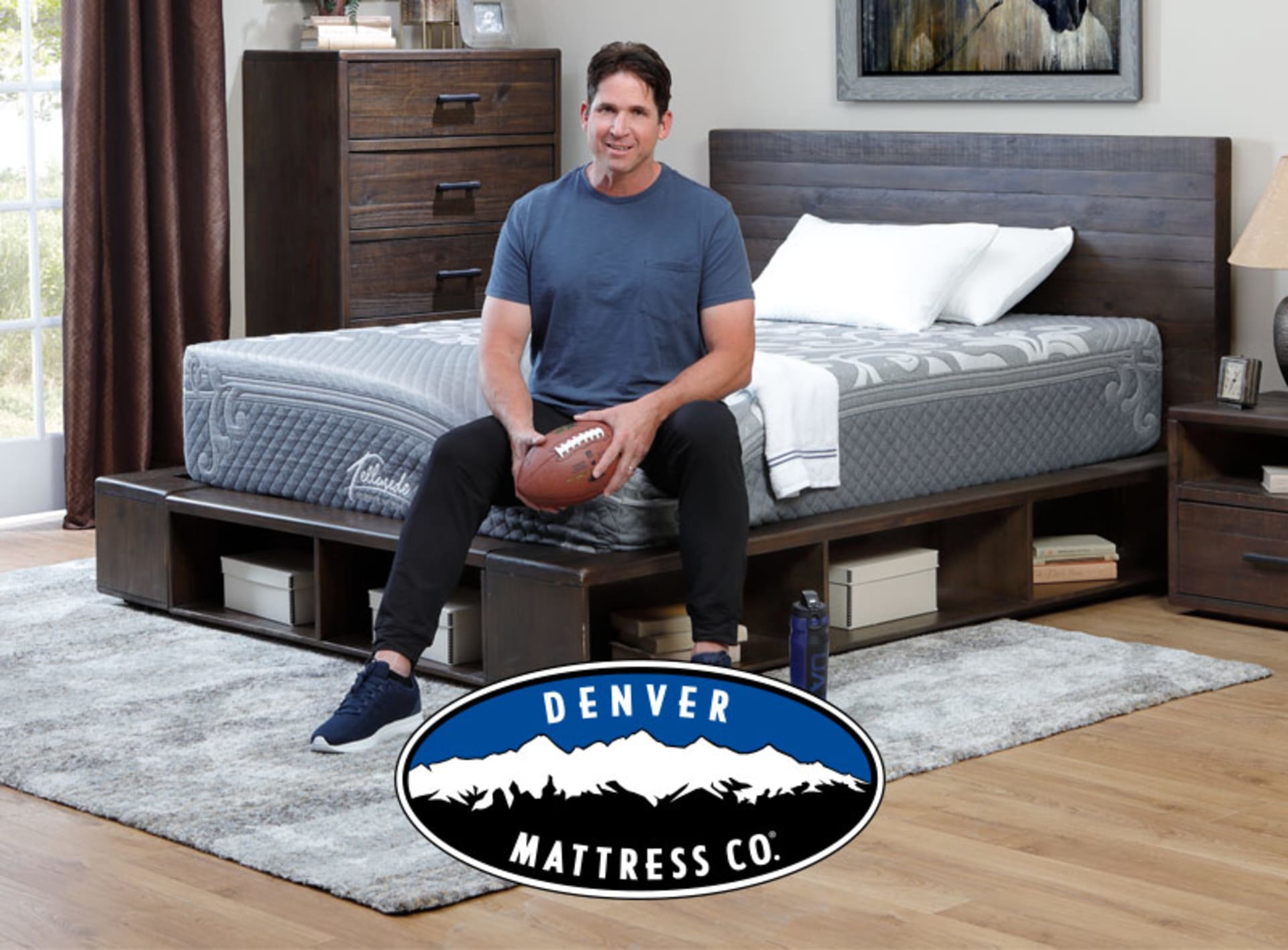 Ed McCaffrey Sitting on Telluride Mattress in Bedroom with football in his hands. Denver Mattress Logo included.