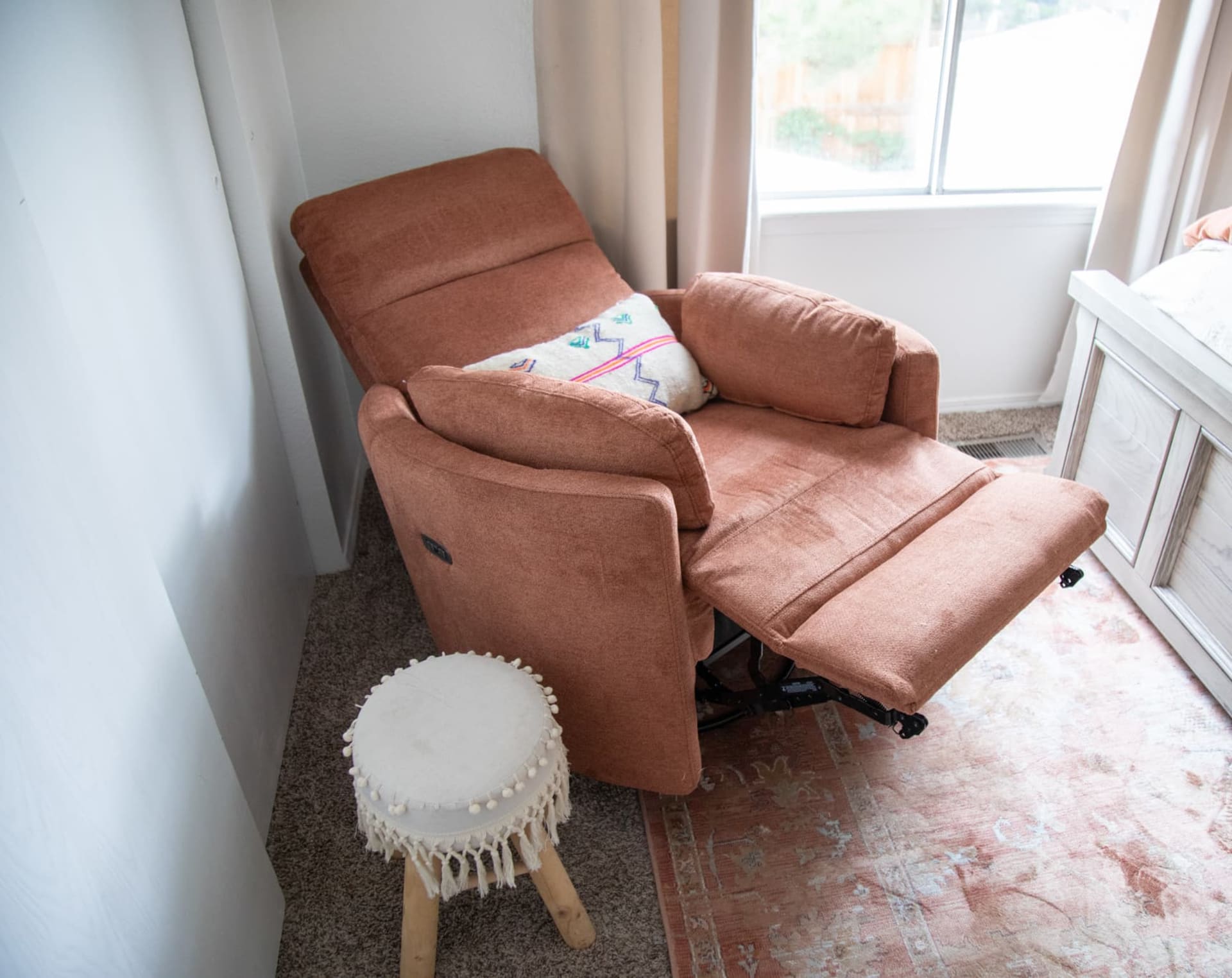 Terracotta colored fabric recliner chair with rounded track arms in a bedroom window scene