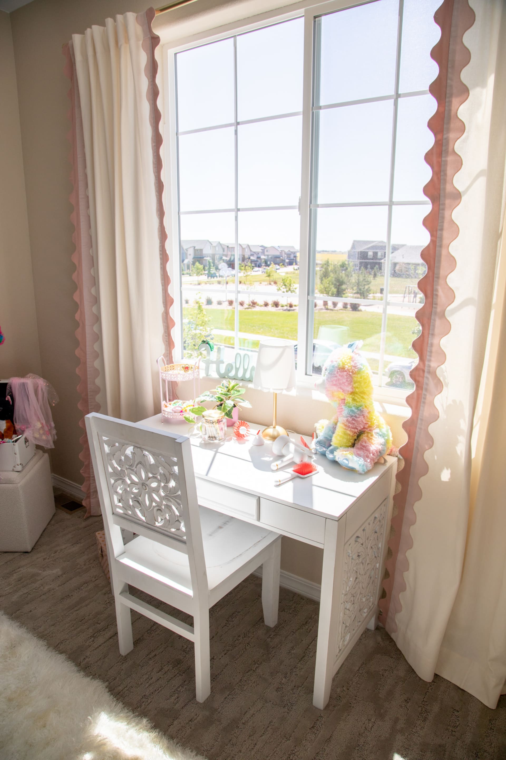 A white writing desk and white wood desk chair with carved detailing by a sunny window