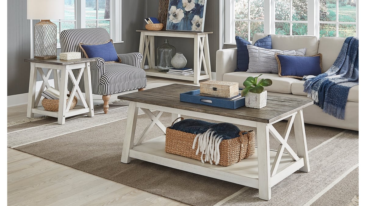 A rectangular coffee table with a white base and brown planked top in a coastal living room