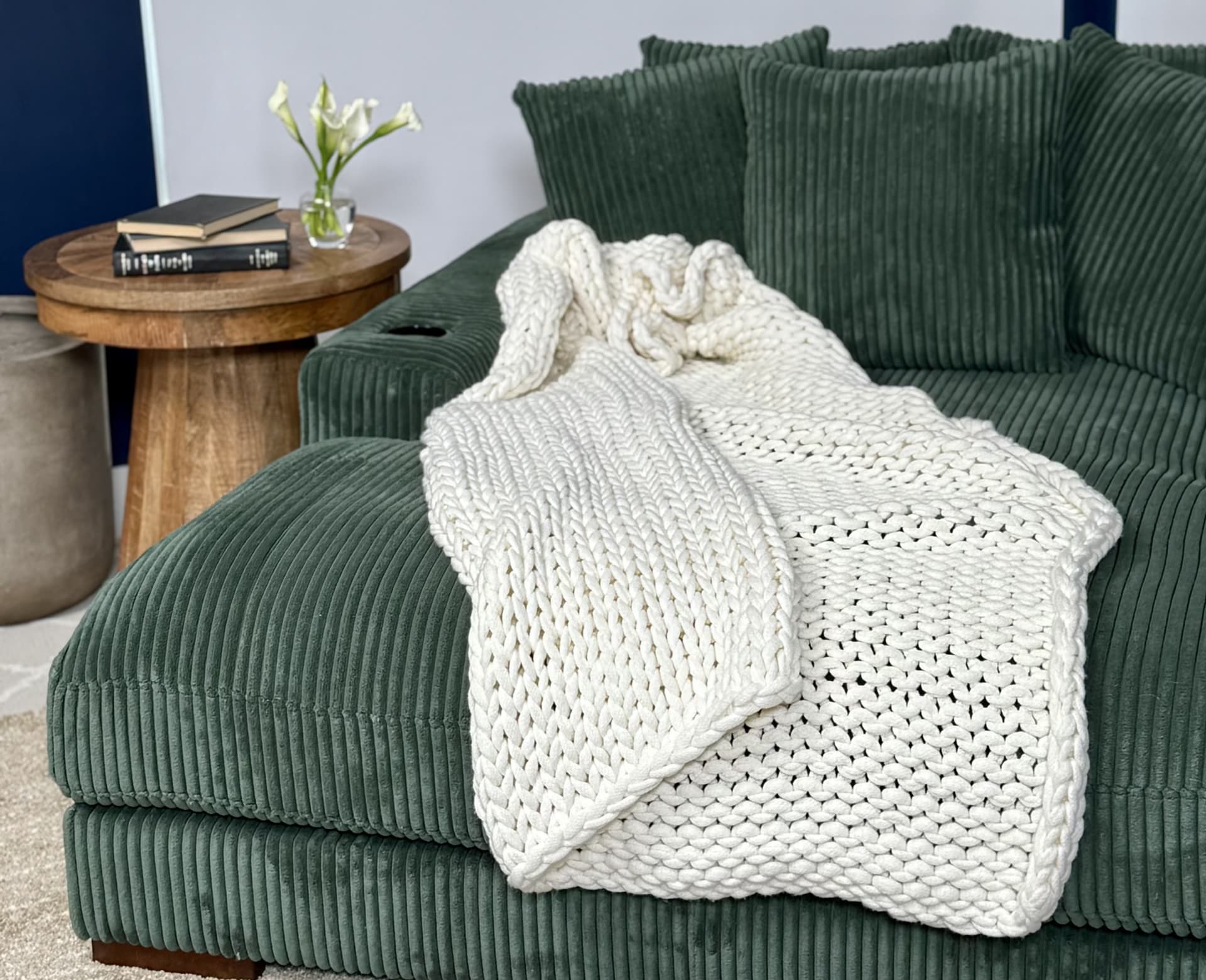 A large chaise lounge with green channeled upholstery with a knit blanket and side table