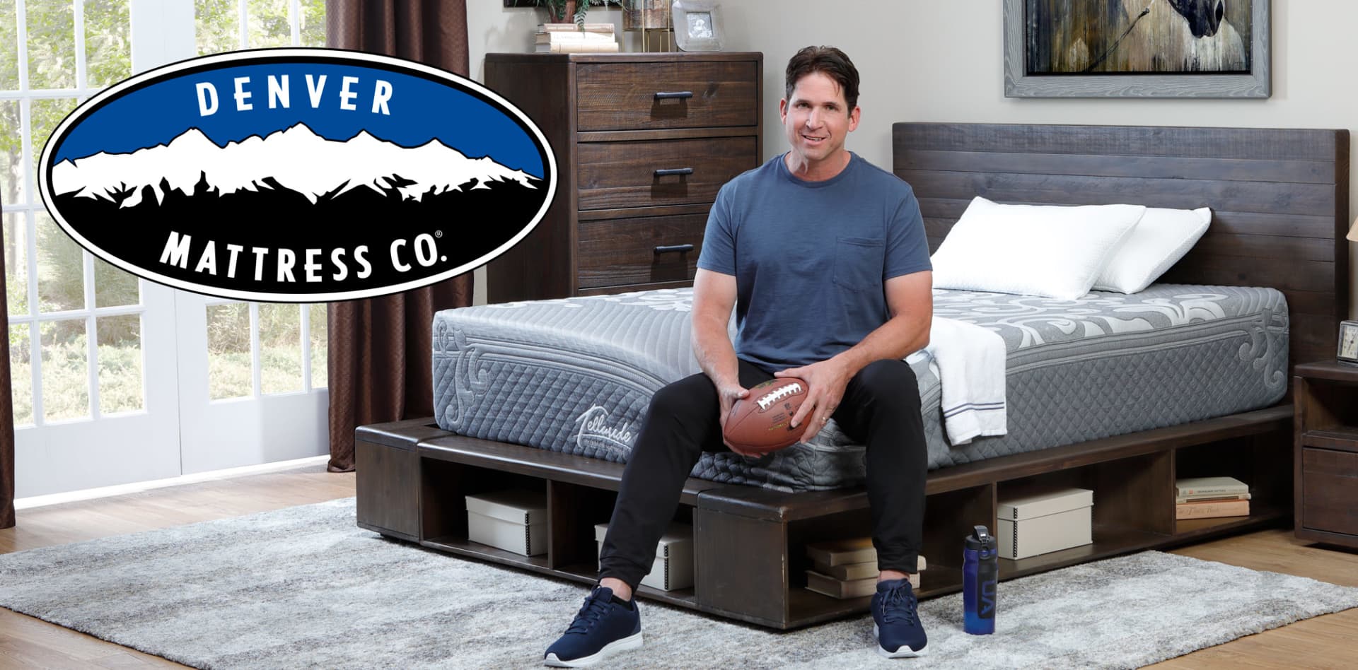 Ed McCaffrey Sitting on Telluride Mattress in Bedroom with football in his hands. Denver Mattress Logo included.